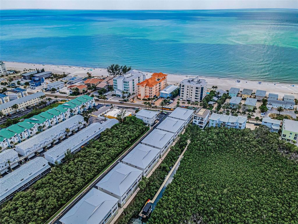 An aerial view shows a row of white townhouses with metal roofs facing a waterway — 19829 GULF BOULEVARD UNIT 501, INDIAN SHORES, FL