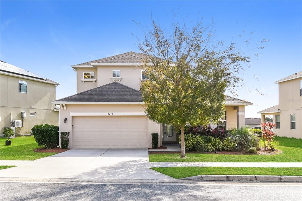 A two-story suburban house features a beige stucco exterior, a two-car garage, and a tree — 2270 NATOMA BOULEVARD, MOUNT DORA, FL
