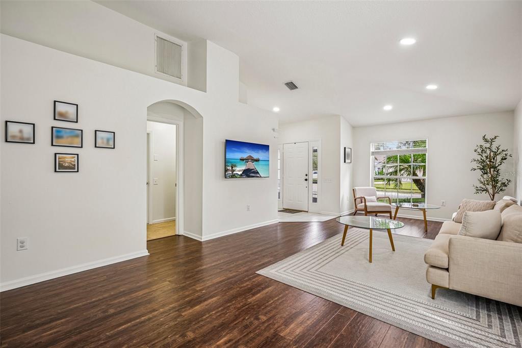 A living room with white walls, dark wood floors, a wall-mounted television, and a sofa — 5854 COUNT TURF LANE, WESLEY CHAPEL, FL