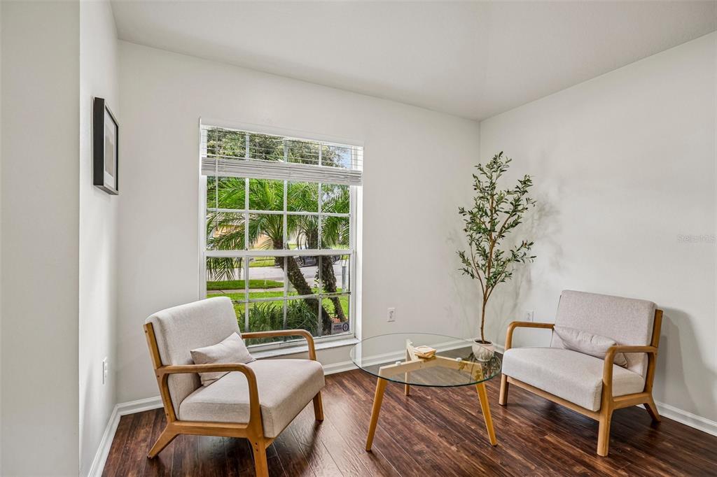 A sunlit sitting area features two light-colored armchairs, a glass coffee table, and wood flooring — 5854 COUNT TURF LANE, WESLEY CHAPEL, FL