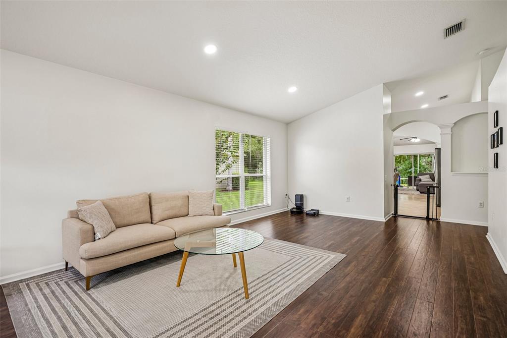 A living room features a beige sofa, glass coffee table, area rug, and dark flooring — 5854 COUNT TURF LANE, WESLEY CHAPEL, FL