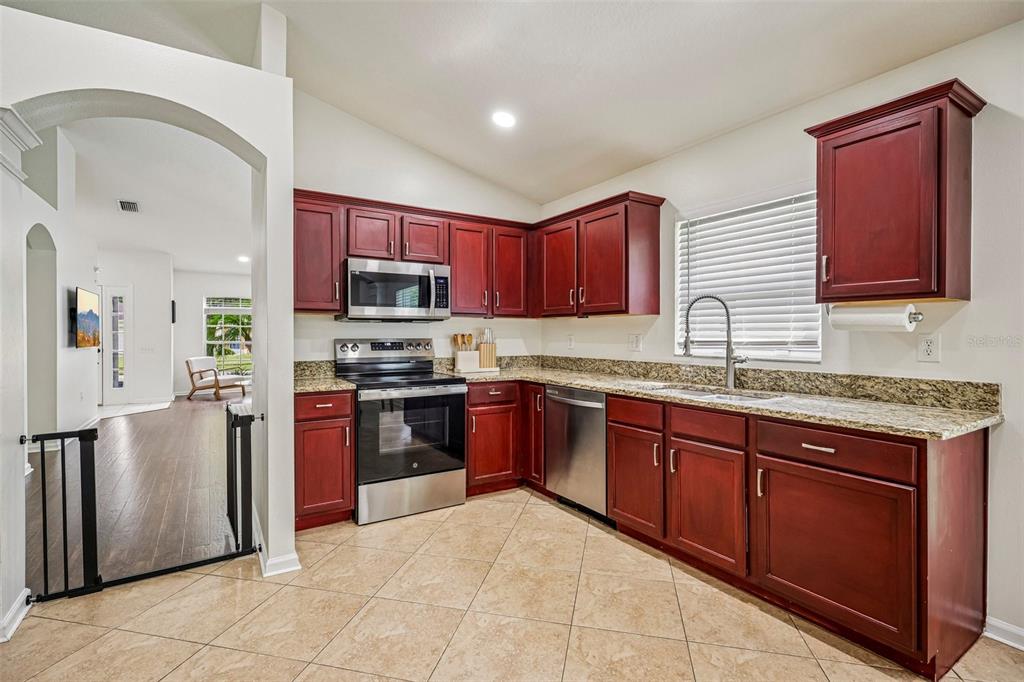 A kitchen with cherry-toned cabinets, granite countertops, stainless steel appliances, and beige tile flooring — 5854 COUNT TURF LANE, WESLEY CHAPEL, FL