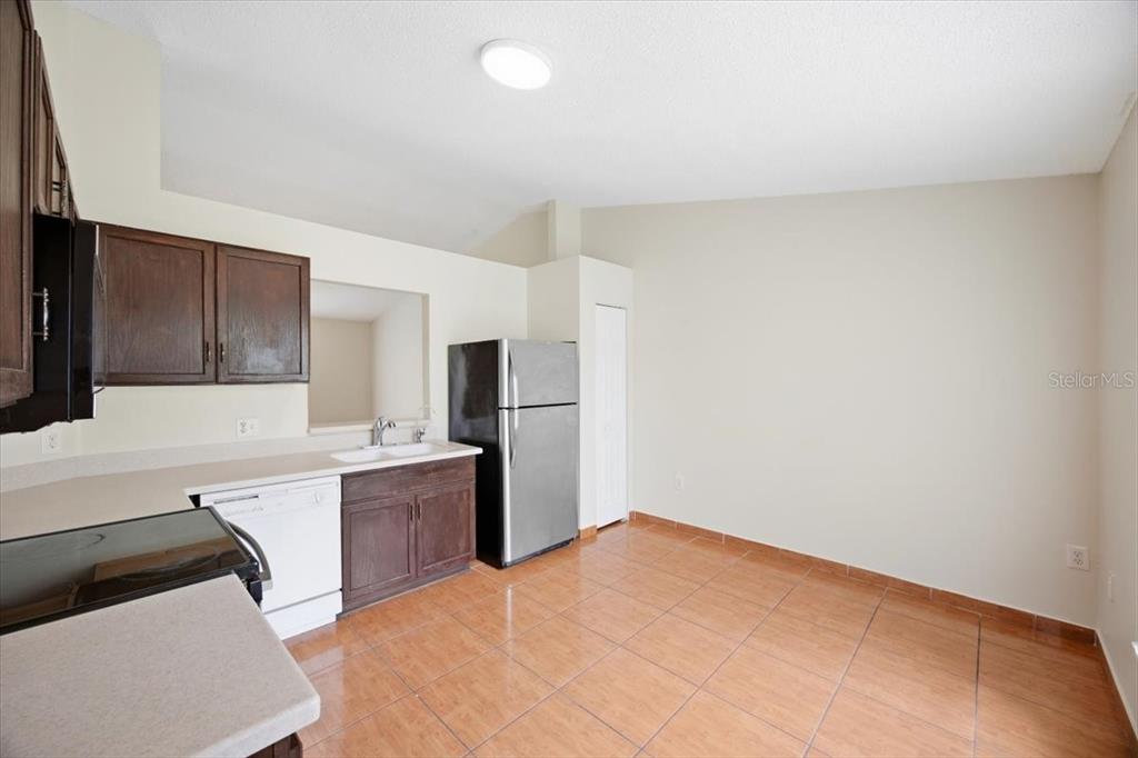 A kitchen with dark wood cabinets, stainless steel appliances, and orange tile flooring — 718 PINCON LANE, KISSIMMEE, FL