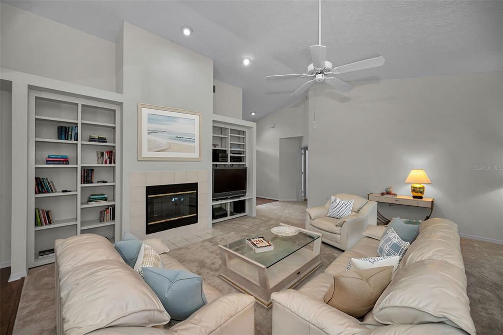 A living room features a fireplace, built-in shelving, a ceiling fan, and neutral-toned furniture — 900 LUCAS LANE, OLDSMAR, FL