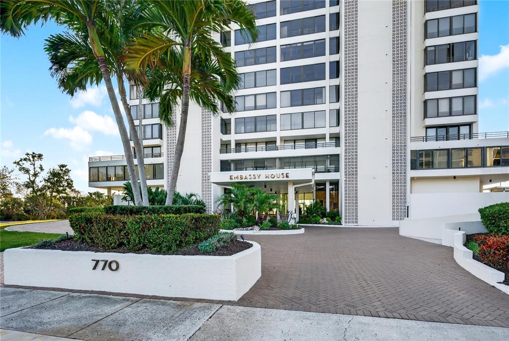 An aerial view shows a tall residential building situated along a coastal road and bay — 770 S PALM AVENUE UNIT PH2, SARASOTA, FL