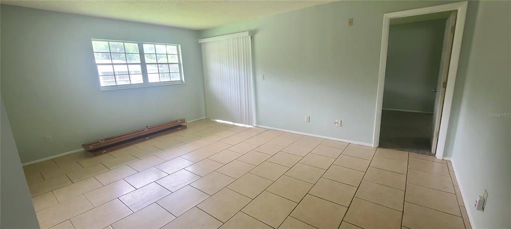 An empty room with light-colored tile flooring, a window, sliding glass doors, and a doorway — 580 FAIRWAYS LANE UNIT G203, OCALA, FL