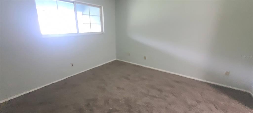 An empty bedroom features light-colored walls, beige carpeting, and a large window with muntins — 580 FAIRWAYS LANE UNIT G203, OCALA, FL