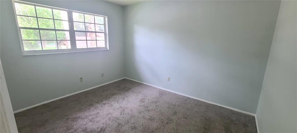 An empty bedroom features light blue walls, gray carpeting, and a large multi-pane window — 580 FAIRWAYS LANE UNIT G203, OCALA, FL