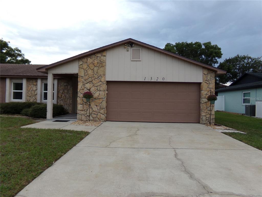 A single-story house with a brown garage door, stone accents, and a side yard — 1320 GLADIOLAS DR, WINTER PARK, FL