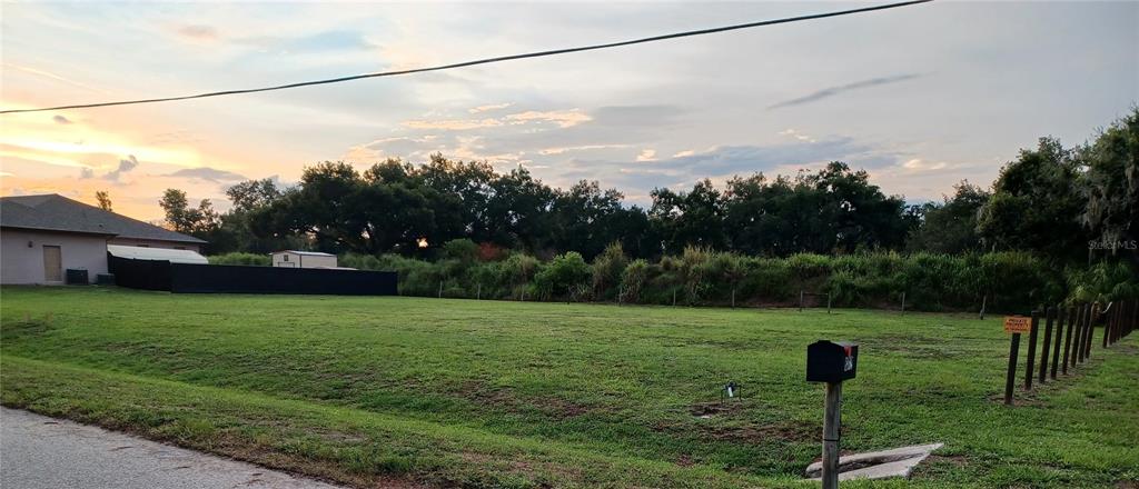 A grassy vacant lot features a mailbox, a fence, and a house in the background — 8310 25TH STREET E, PARRISH, FL