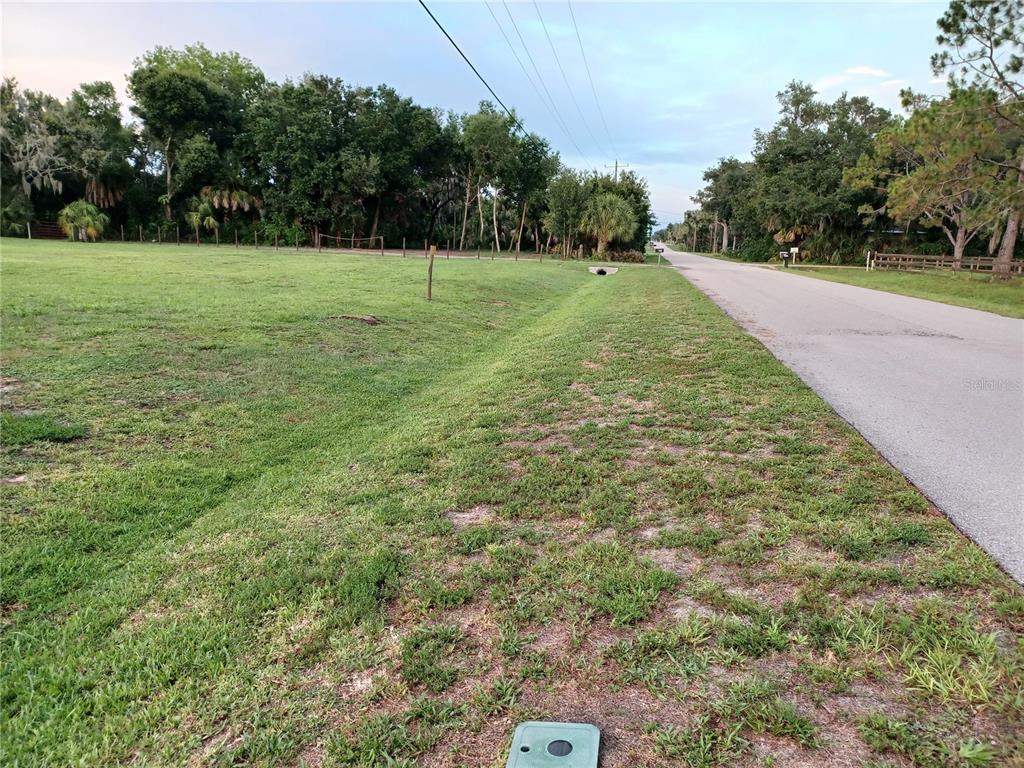 A grassy lot with a drainage ditch runs alongside a paved road near trees — 8310 25TH STREET E, PARRISH, FL