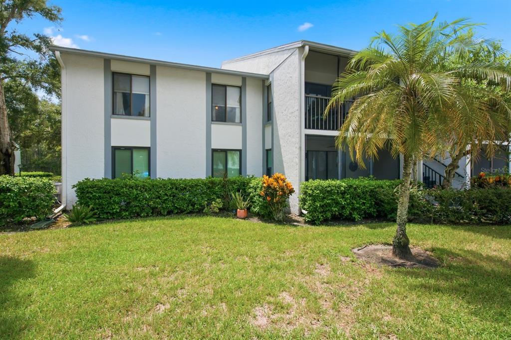 A two-story white apartment building with a screened balcony and a palm tree in front — 1345 PINE RIDGE CIRCLE E UNIT A2, TARPON SPRINGS, FL