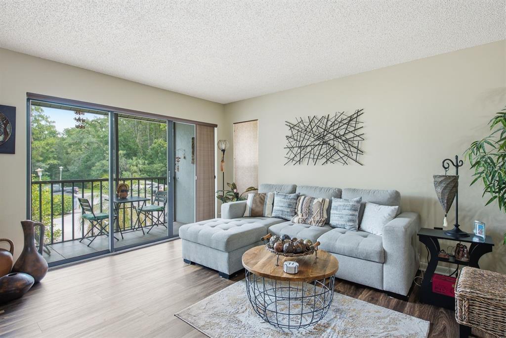 A living room features a grey sectional sofa, a round coffee table, and a balcony view — 1345 PINE RIDGE CIRCLE E UNIT A2, TARPON SPRINGS, FL