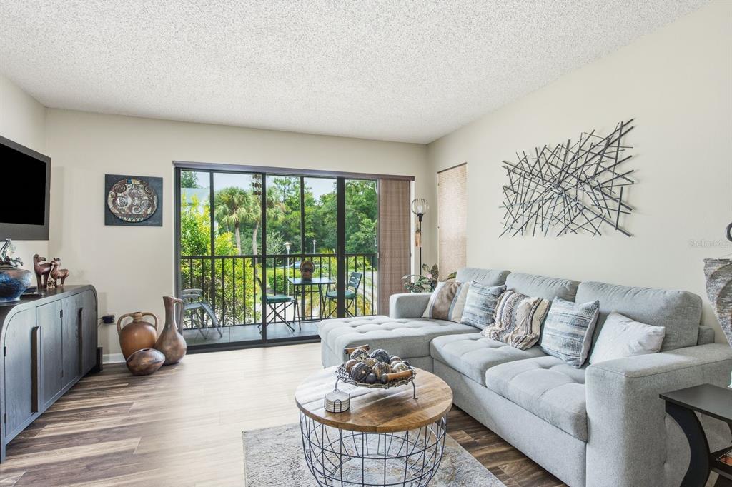 A living room features a gray sectional sofa, a round coffee table, and a balcony view — 1345 PINE RIDGE CIRCLE E UNIT A2, TARPON SPRINGS, FL