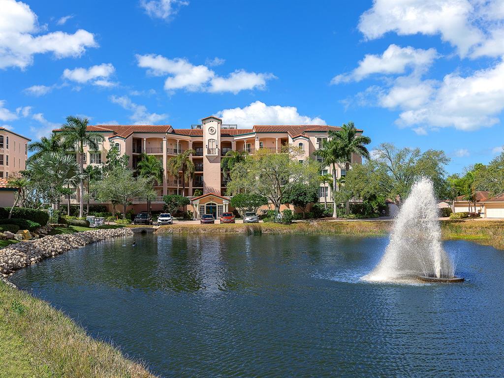 A multi-story apartment building stands behind a pond with a large water fountain — 5420 EAGLES POINT CIRCLE UNIT 106, SARASOTA, FL