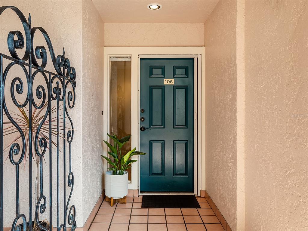 A teal front door with number 106 is situated in a tiled entryway with wrought-iron decor — 5420 EAGLES POINT CIRCLE UNIT 106, SARASOTA, FL