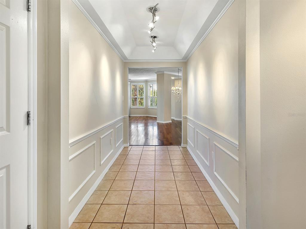 A tiled hallway with wainscoting leads to a room with hardwood floors and large windows — 5420 EAGLES POINT CIRCLE UNIT 106, SARASOTA, FL