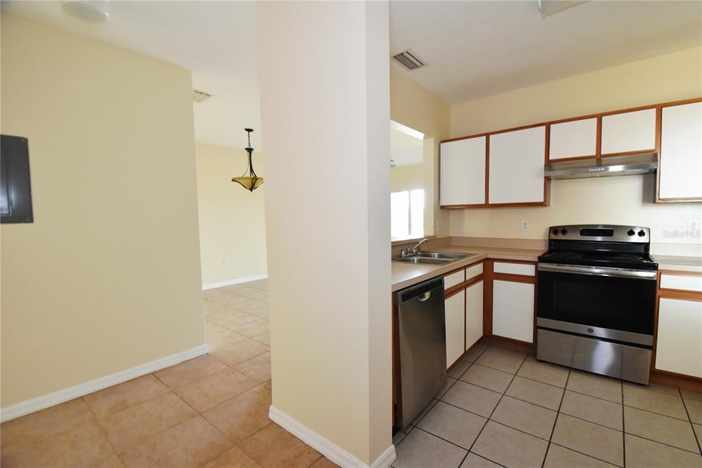 A kitchen with white cabinets, stainless steel appliances, and tile flooring opens to a dining area — 9612 SEADALE COURT UNIT 201, RIVERVIEW, FL