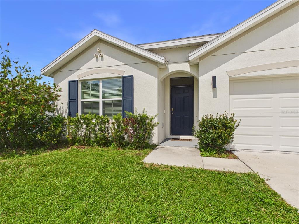 A single-story house exterior features a dark blue front door, white stucco walls, and shutters — 149 HICKORY COURSE CIRCLE, OCALA, FL