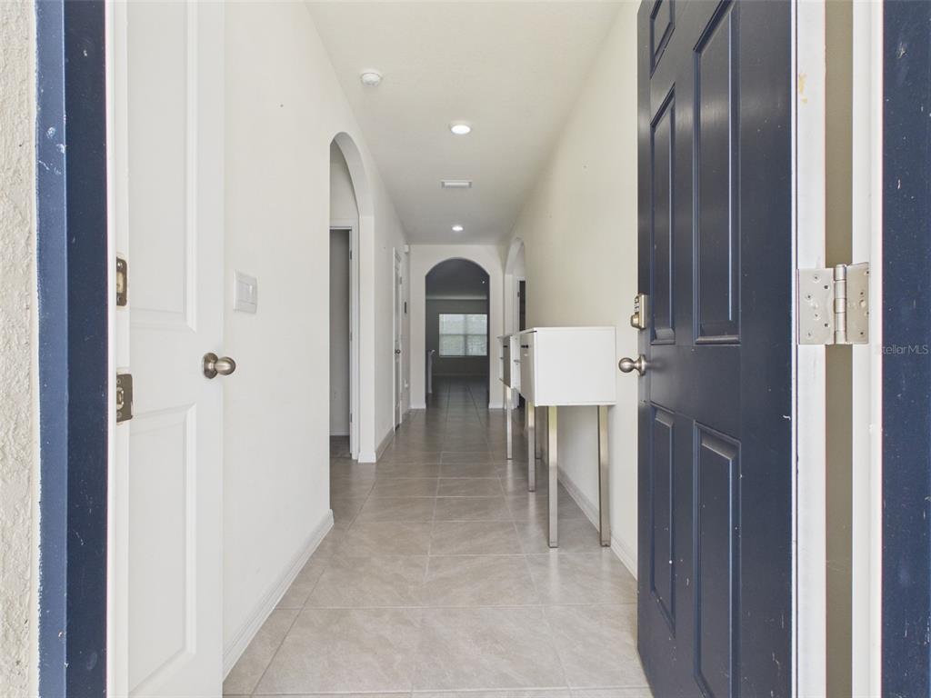 A view through an open dark blue door into a tiled hallway with arched doorways — 149 HICKORY COURSE CIRCLE, OCALA, FL