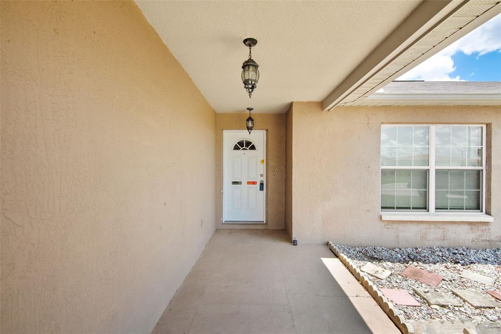 A covered entryway features a white front door, a beige stucco wall, and a window — 8425 CORNEY DRIVE, PORT RICHEY, FL