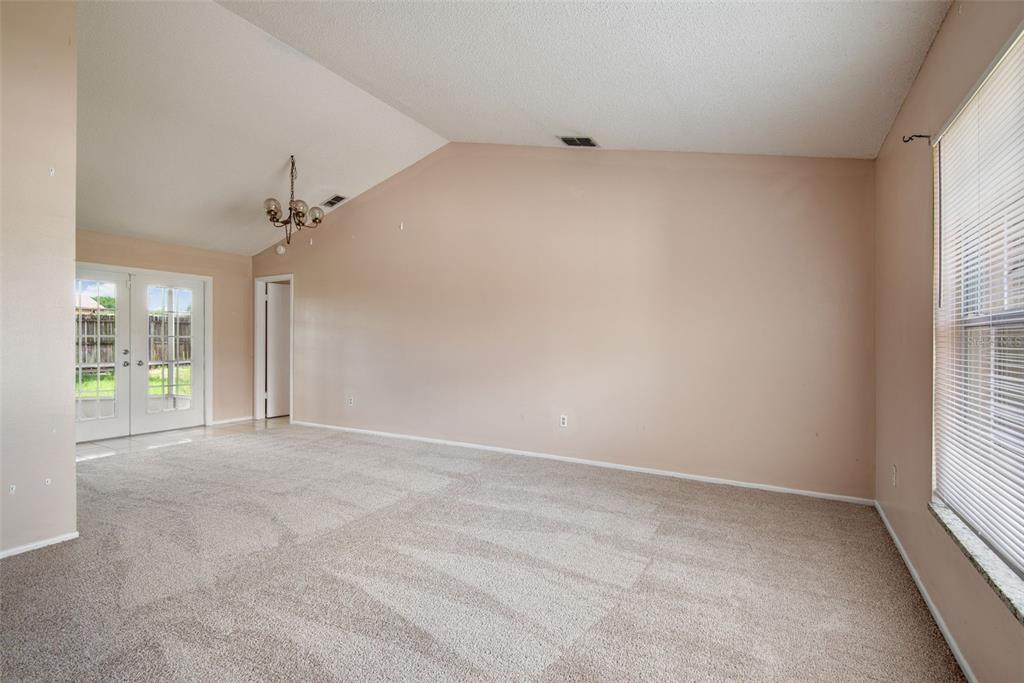 An empty living room features beige walls, vaulted ceilings, carpeted floors, and glass patio doors — 8425 CORNEY DRIVE, PORT RICHEY, FL