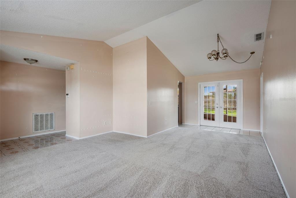 A living room with beige walls, gray carpeting, a vaulted ceiling, and glass French doors — 8425 CORNEY DRIVE, PORT RICHEY, FL
