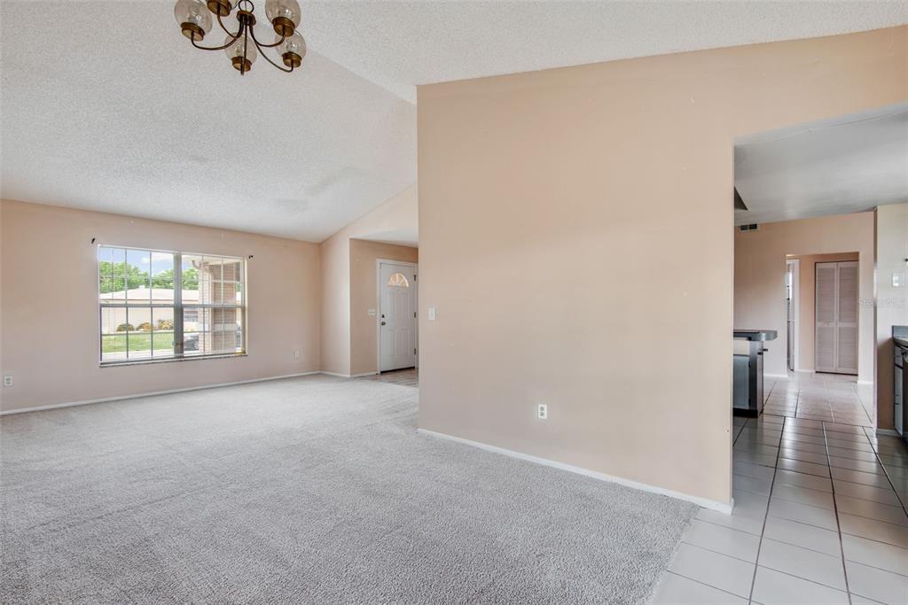 A living room with beige walls, gray carpeting, a vaulted ceiling, and a tile-floored entryway — 8425 CORNEY DRIVE, PORT RICHEY, FL