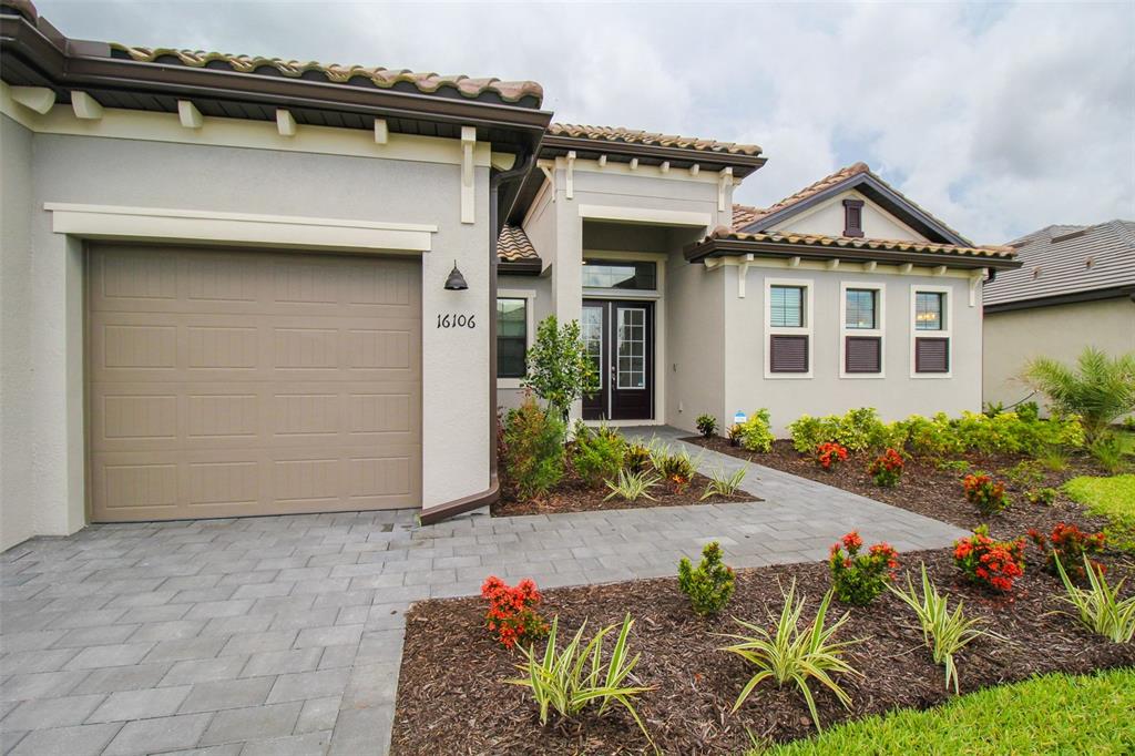 A single-story house exterior features a beige stucco facade, a tiled roof, and a paver driveway — 16106 TRADEWIND TERRACE, BRADENTON, FL