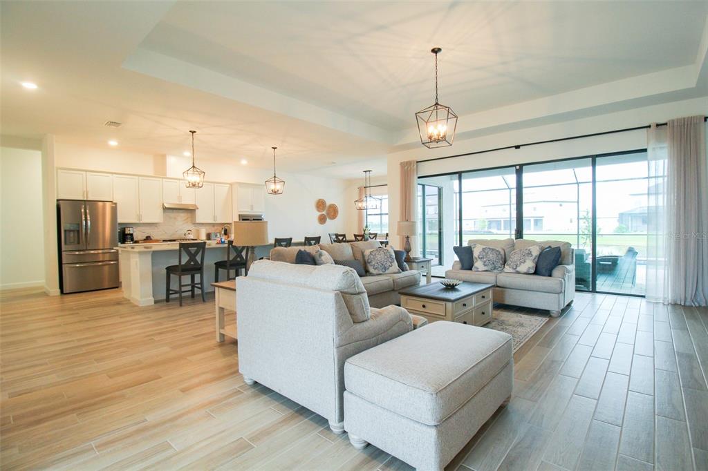 An open-concept living room and kitchen featuring light wood-look tile floors and sliding glass doors — 16106 TRADEWIND TERRACE, BRADENTON, FL