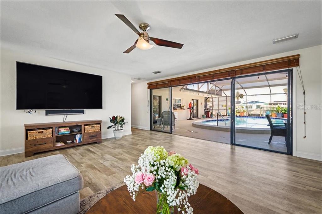 A living room with wood-look flooring opens through sliding glass doors to a screened pool — 124 ANCHOR DRIVE, PONCE INLET, FL