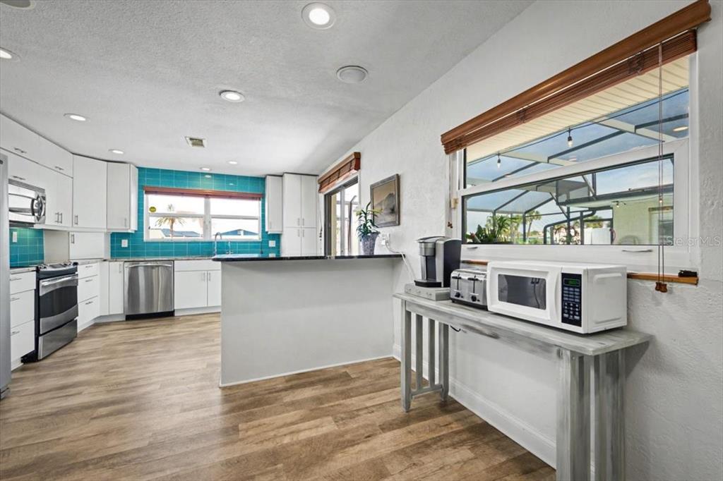 A kitchen features white cabinets, a teal tiled backsplash, wood-look flooring, and a breakfast bar — 124 ANCHOR DRIVE, PONCE INLET, FL