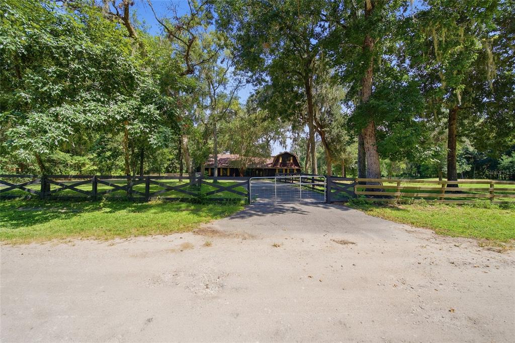 A gated driveway leads to a house nestled among mature trees behind a wooden fence — 22289 CHERATON ROAD, BROOKSVILLE, FL
