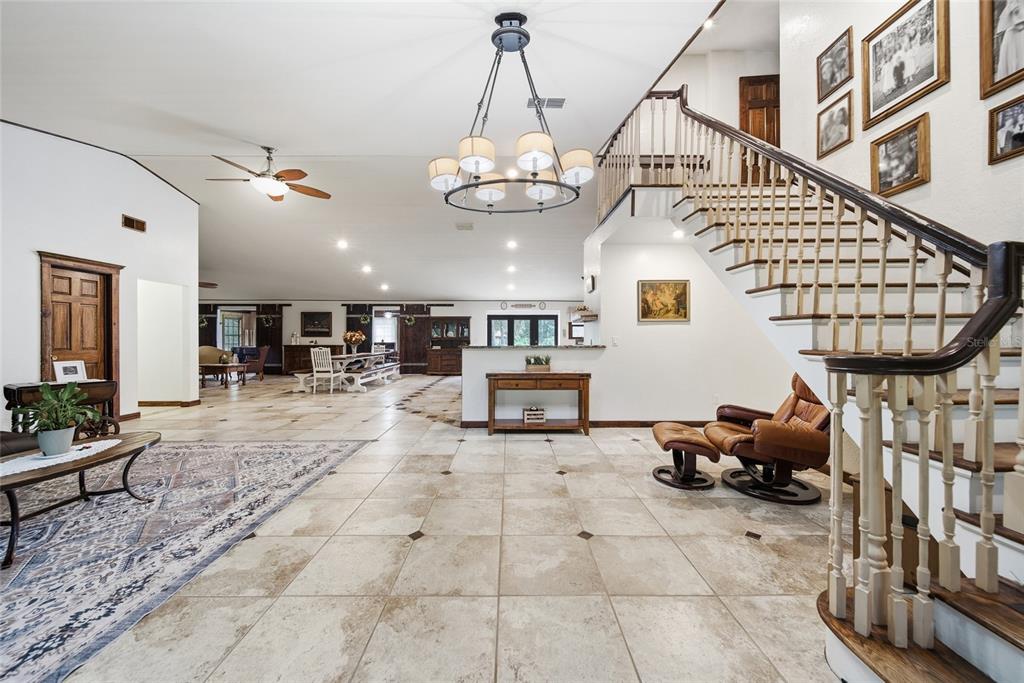 A spacious living area features tile flooring, a staircase with wooden railings, and a chandelier — 22289 CHERATON ROAD, BROOKSVILLE, FL
