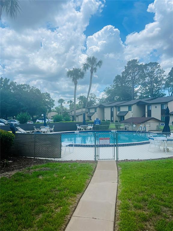 A fenced outdoor swimming pool with lounge chairs and palm trees in front of apartment buildings — 625 MIDWAY DRIVE UNIT B, OCALA, FL