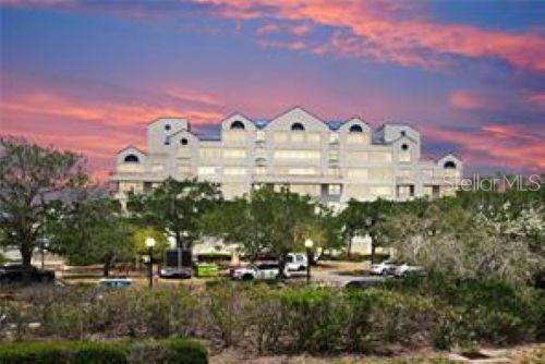 A multi-story apartment building stands behind trees under a vibrant sunset sky — 2333 FEATHER SOUND DRIVE UNIT B304, CLEARWATER, FL