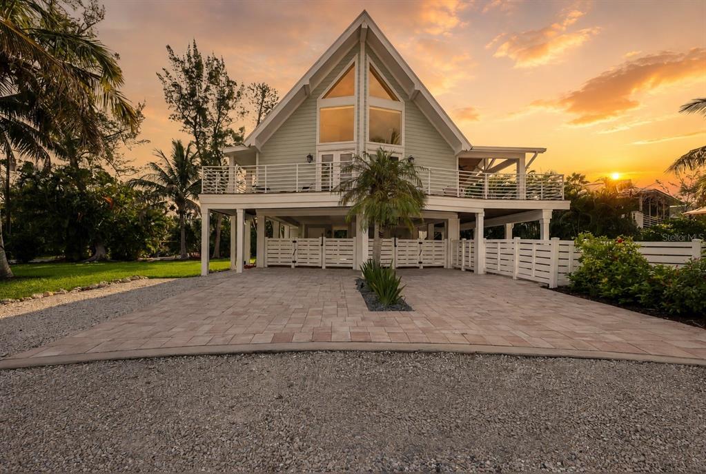 An elevated A-frame house with a paved driveway and a wraparound deck at sunset — 315 HAMMOCK CIRCLE, ANNA MARIA, FL