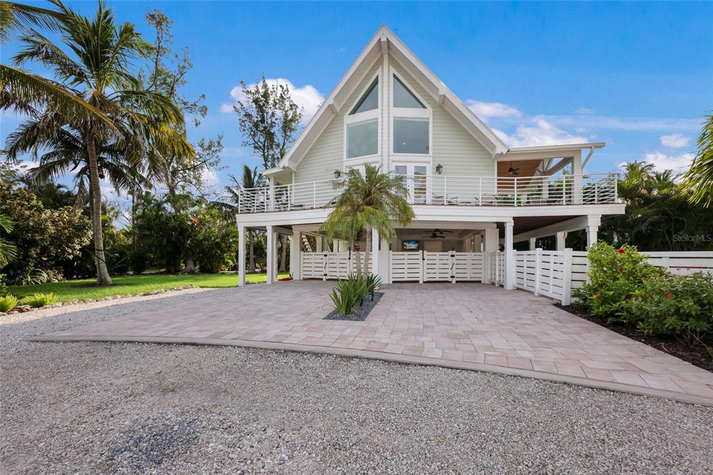 A stilt-elevated house with a pale green exterior, a large deck, and a paved driveway — 315 HAMMOCK CIRCLE, ANNA MARIA, FL