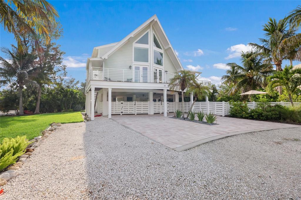 A stilt house with a white exterior, a balcony, and a paved driveway with palm trees — 315 HAMMOCK CIRCLE, ANNA MARIA, FL