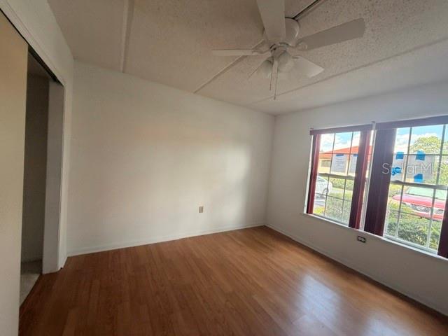 An empty bedroom features wood-look flooring, a ceiling fan, and windows overlooking a parking area — 2400 FOREST DRIVE UNIT 103, INVERNESS, FL