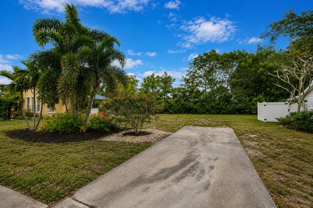 A concrete driveway leads toward a grassy backyard with palm trees and dense perimeter foliage — 463 ACACIA DRIVE, SARASOTA, FL