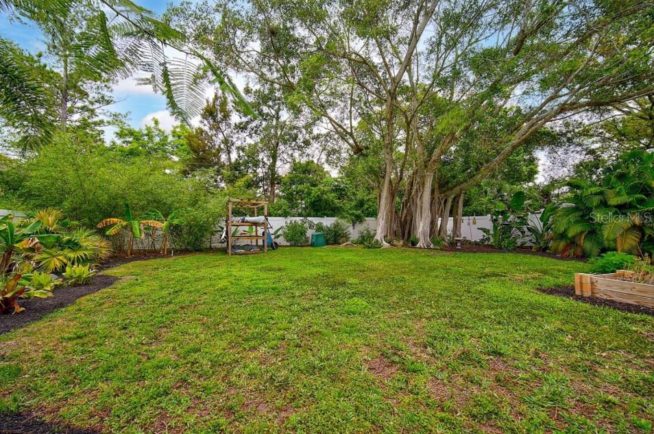 A grassy backyard features a wooden storage rack, mature trees, and a white privacy fence — 463 ACACIA DRIVE, SARASOTA, FL