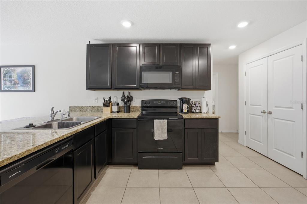 A kitchen features dark cabinets, granite countertops, black appliances, and light tile flooring — 273 HICKORY COURSE RADIAL, OCALA, FL