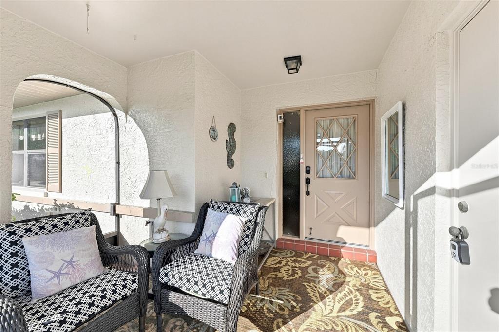 A covered front porch features two wicker chairs, a patterned rug, and a tan door — 1618 LAYTON COURT, SUN CITY CENTER, FL