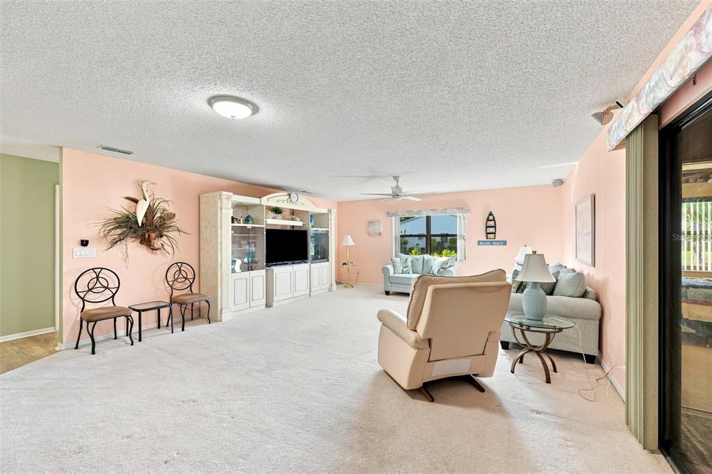 A living room features peach walls, white carpet, a large entertainment center, and beige furniture — 1618 LAYTON COURT, SUN CITY CENTER, FL