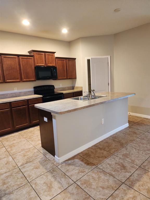 A kitchen features dark wood cabinets, a central island with a sink, and tiled flooring — 2765 CARRICKTON CIRCLE, ORLANDO, FL