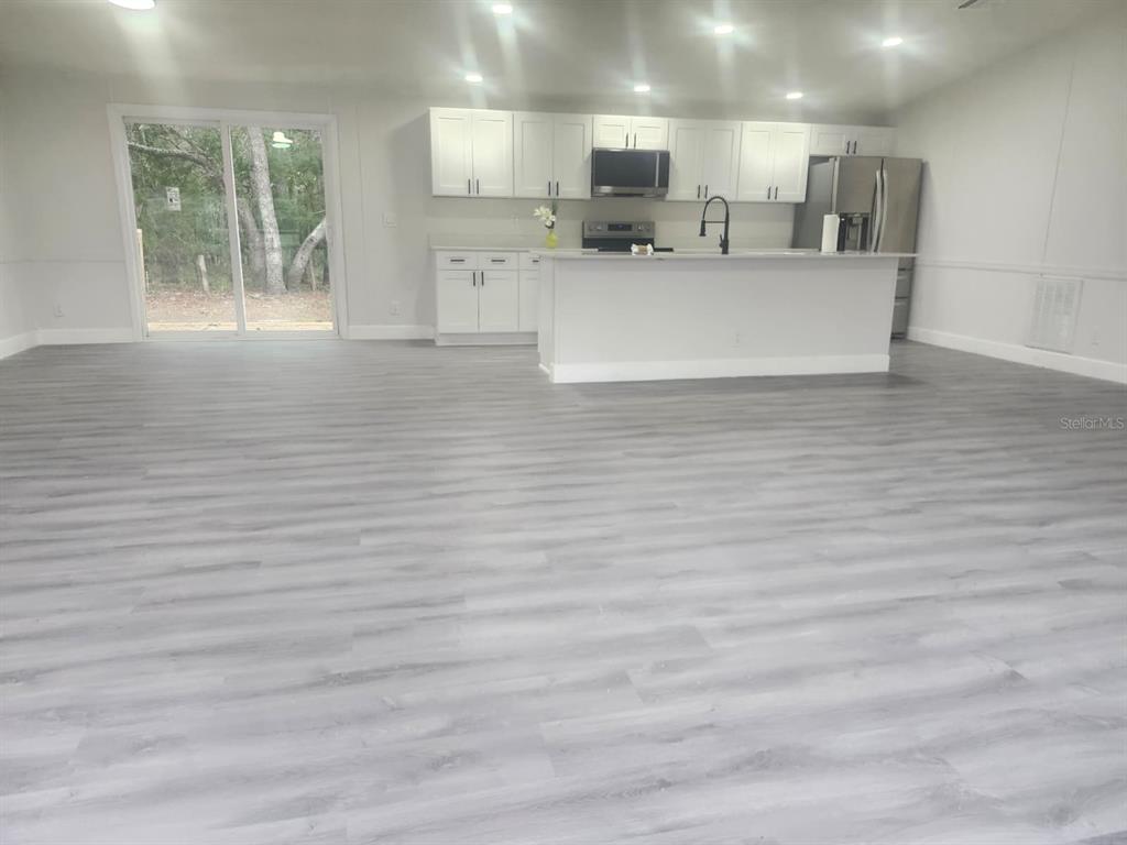 A modern kitchen features white cabinets, a central island, and light gray wood-look flooring — 5641 & 5685 S. BUTAN POINT, HOMOSASSA, FL