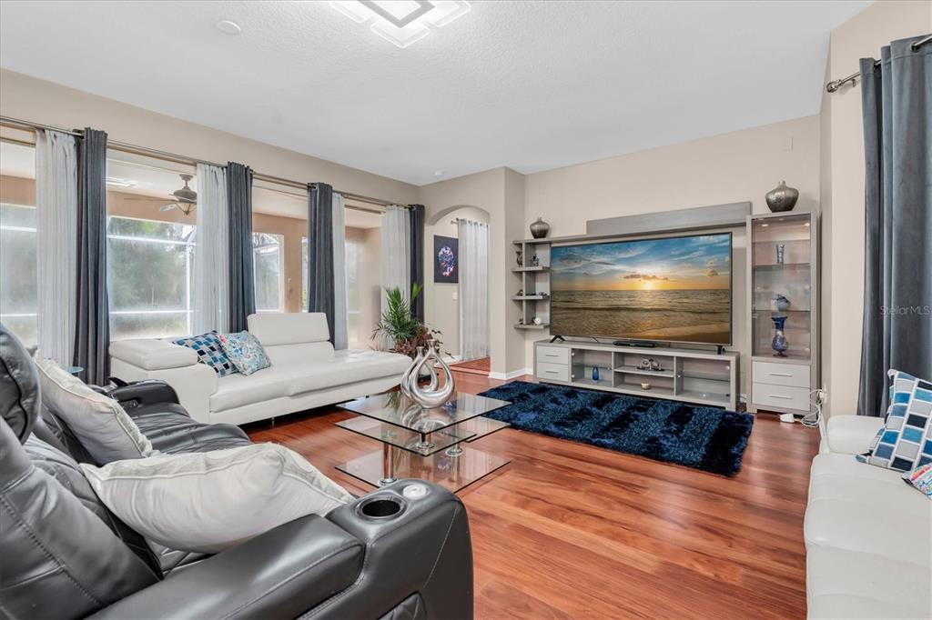 A living room features a large television, white sofas, a glass coffee table, and wood flooring — 10436 CANARY ISLE DRIVE, TAMPA, FL