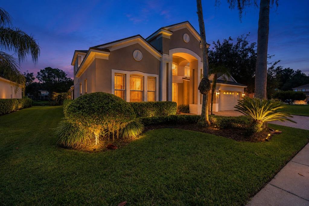 A two-story house with a beige exterior, arched entryway, and illuminated landscaping at dusk — 10436 CANARY ISLE DRIVE, TAMPA, FL