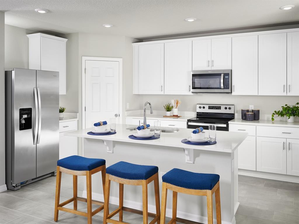 A modern kitchen features white cabinetry, stainless steel appliances, a quartz island, and blue stools — 2875 HORNBILL DRIVE, ST CLOUD, FL